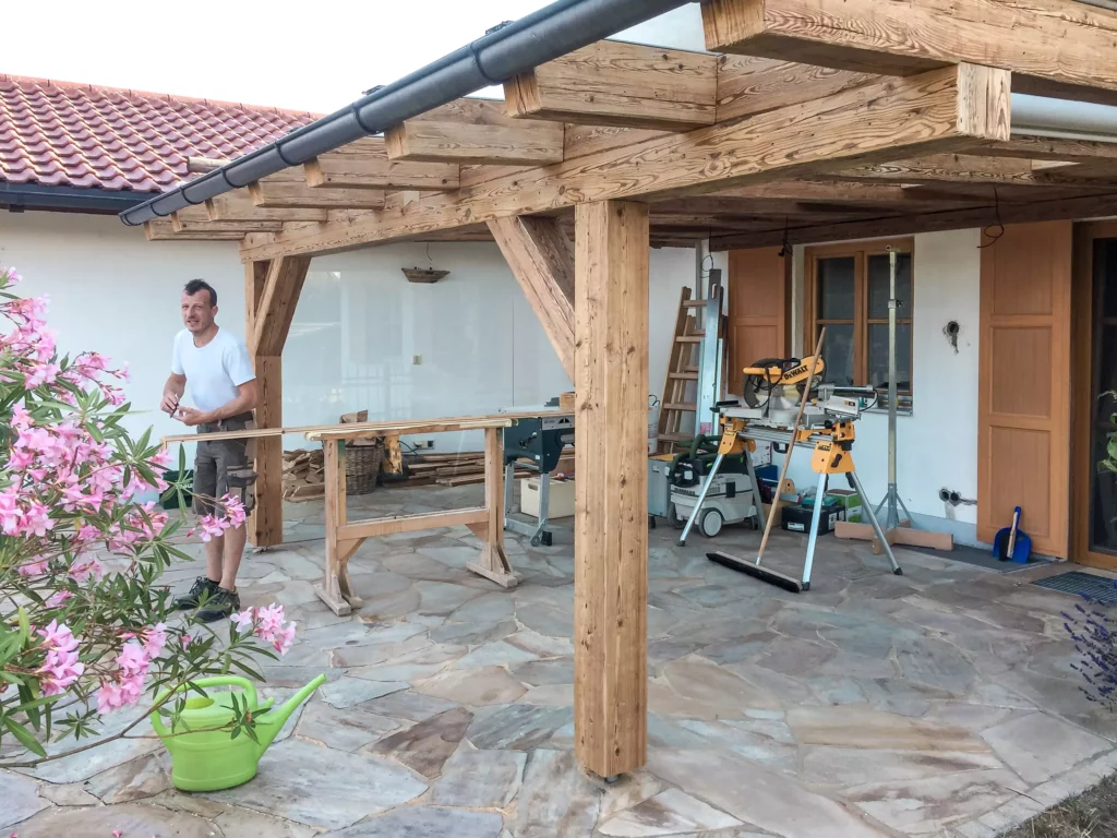 Tischler arbeitet unter überdachtem Außenbereich mit Altholzverbau und Werkzeugen für maßgefertigte Möbel in, Altholzmöbel