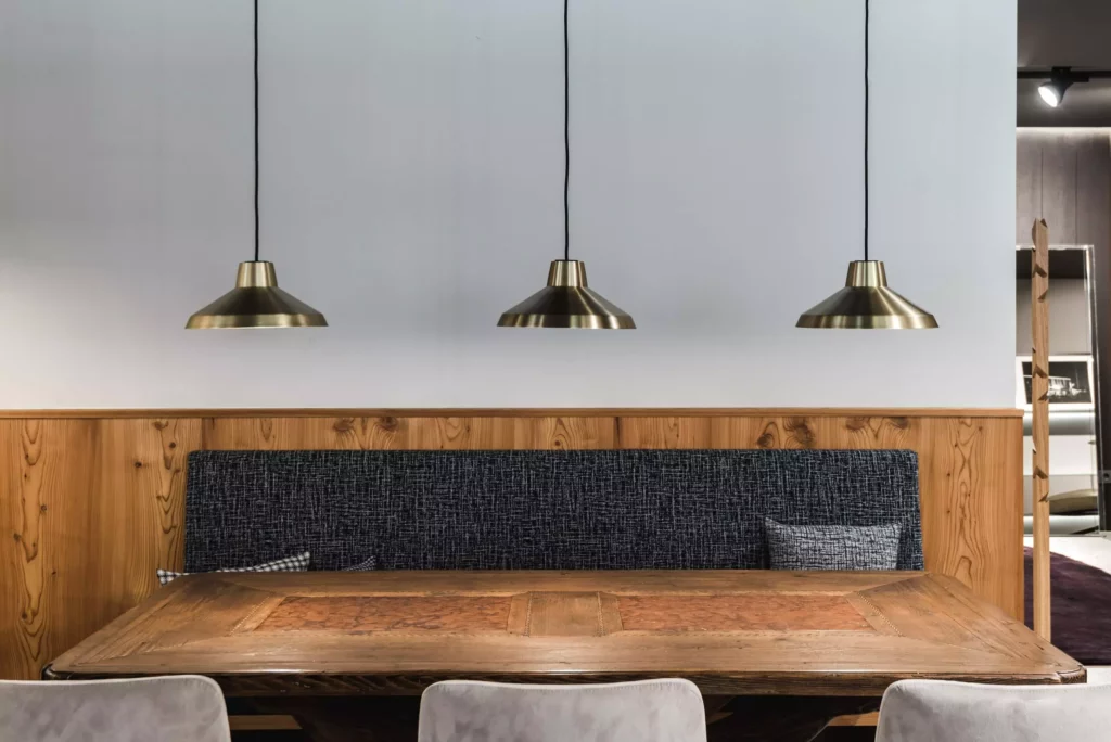 Moderner Showroom mit maßgefertigtem Holztisch, gepolsterter Sitzbank, Holzverkleidung und drei hängenden Messinglampen