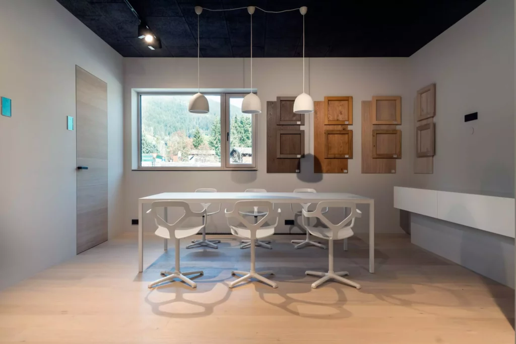 Moderner Showroom mit weißem Tisch, sechs weißen Designstühlen, Holzmustern an der Wand und großem Fenster mit Bergblick