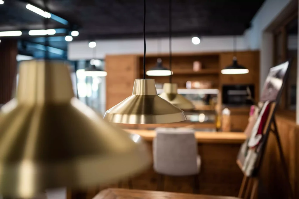 Nahaufnahme von goldfarbenen Pendelleuchten in einem modernen Möbelstudio-Showroom mit Holzvertäfelung und Sitzbereich im