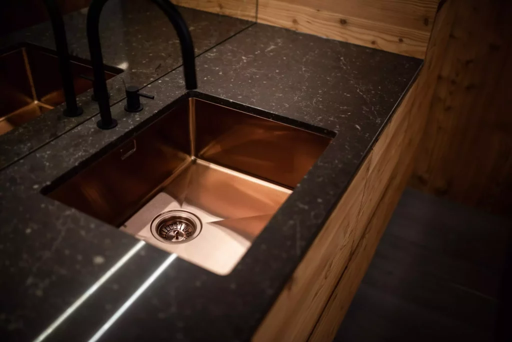 Kupferfarbene Spüle mit schwarzem Wasserhahn in maßgefertigter Holzarbeitsplatte und dunkler Stein-Arbeitsfläche im Showroom