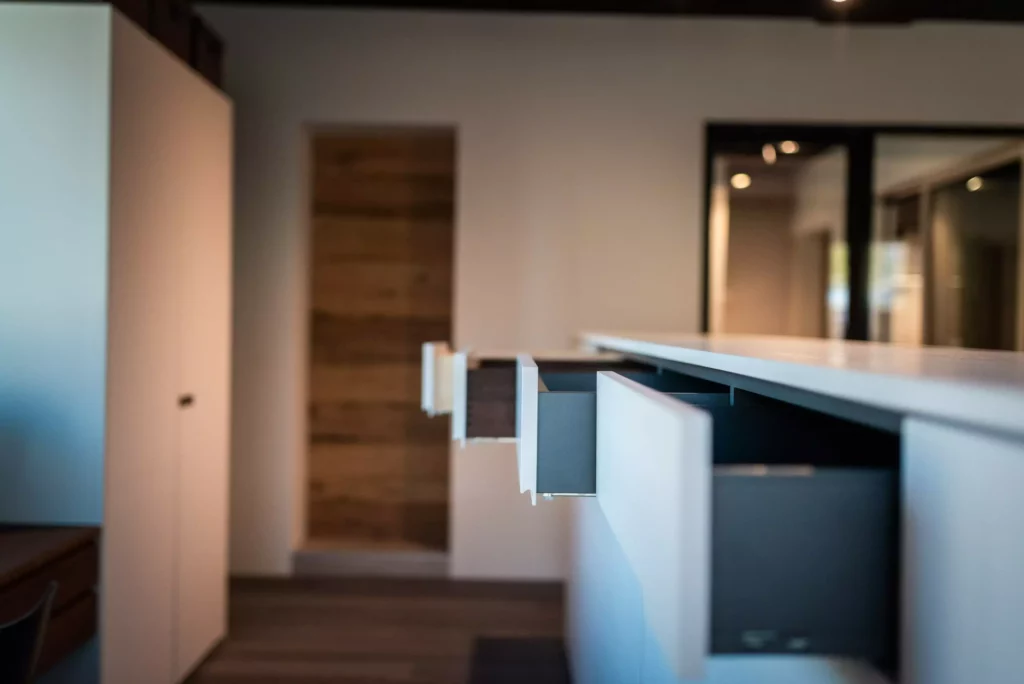 Offene Schubladen einer modernen weißen Kücheninsel im Showroom mit Holzfußboden und minimalistischer Innenarchitektur