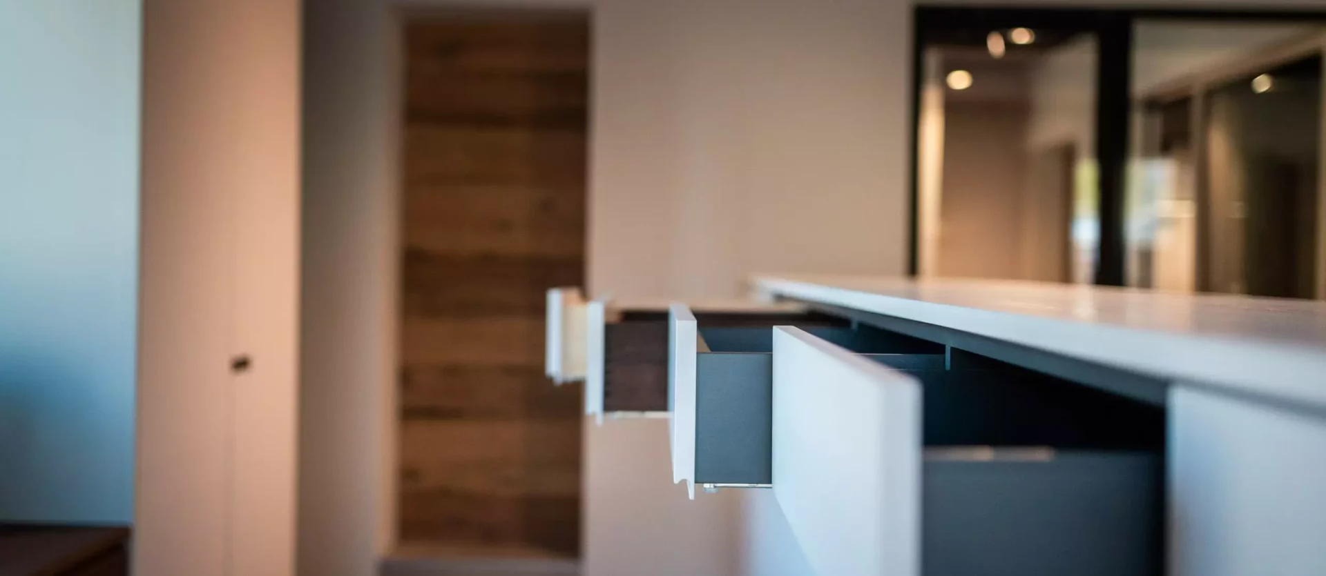 Offene Schubladen einer modernen weißen Kücheninsel im Showroom mit Holzfußboden und minimalistischer Innenarchitektur