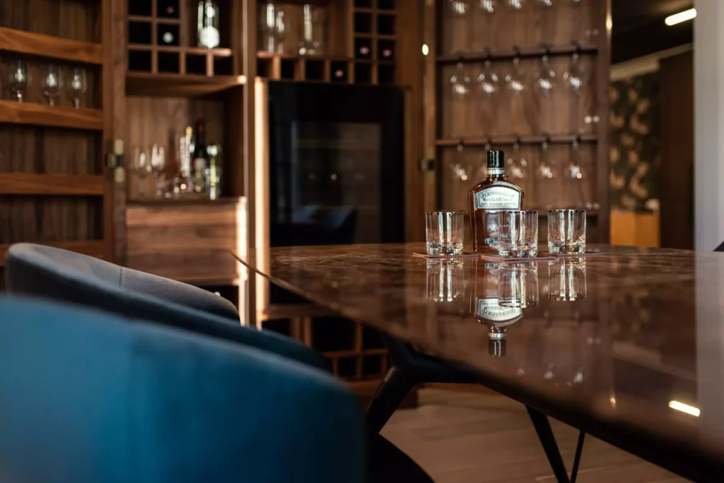 Moderner Showroom mit poliertem Holztisch, blauen Stühlen, Flaschendekor und Gläsern vor maßgefertigten Holzregalen für Wein