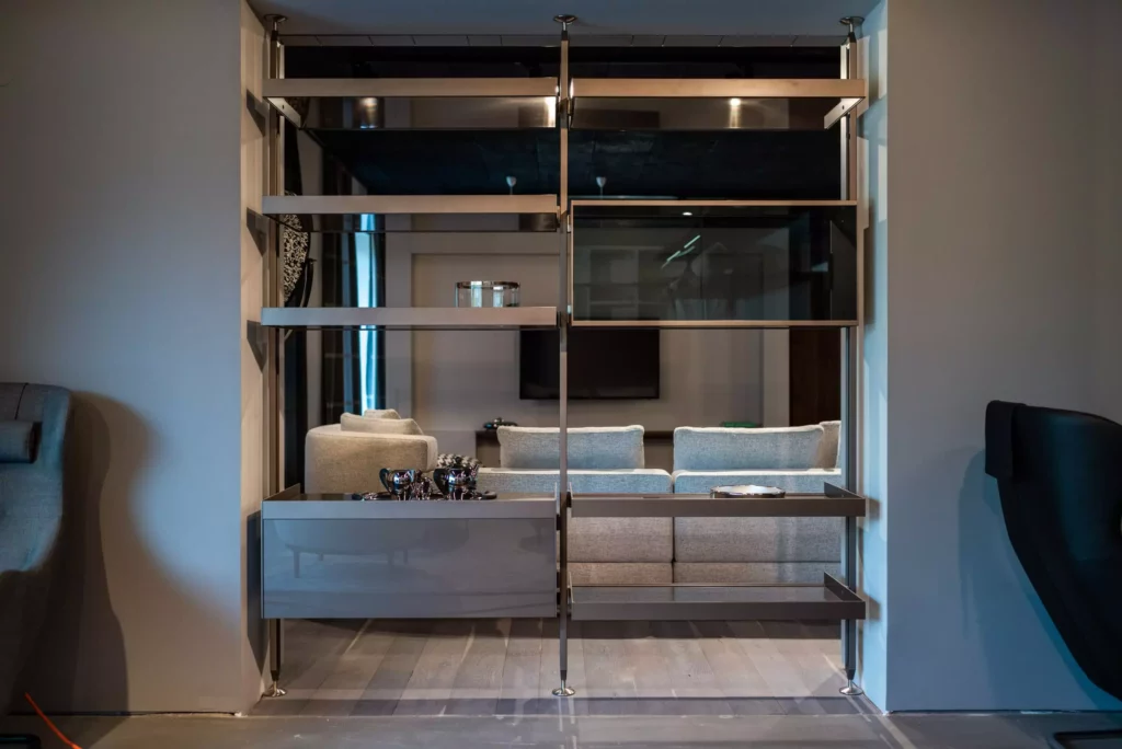 moderner showroom mit offenem raumkonzept, graues regal mit metallrahmen, sicht auf graues sofa und wandfernseher