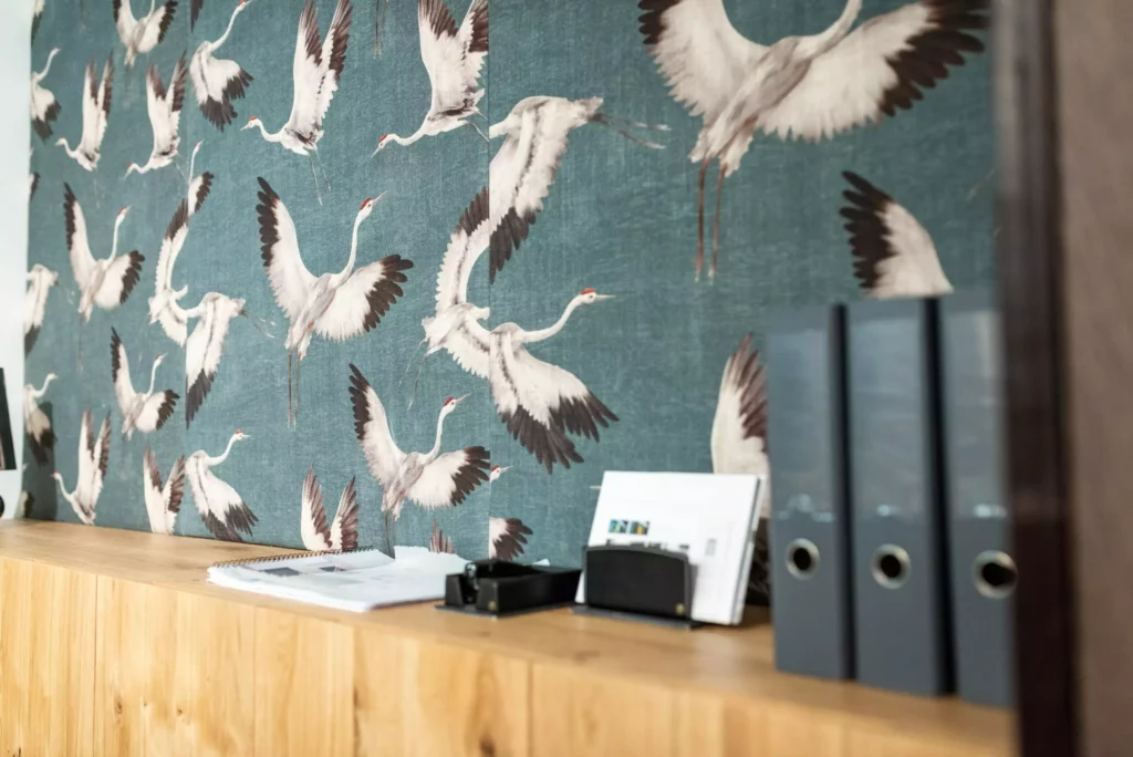 Holzsideboard vor Wand mit Kranich-Vogel-Tapete, darauf Ordner, Papiere und Büro-Organizer im Möbelstudio Showroom