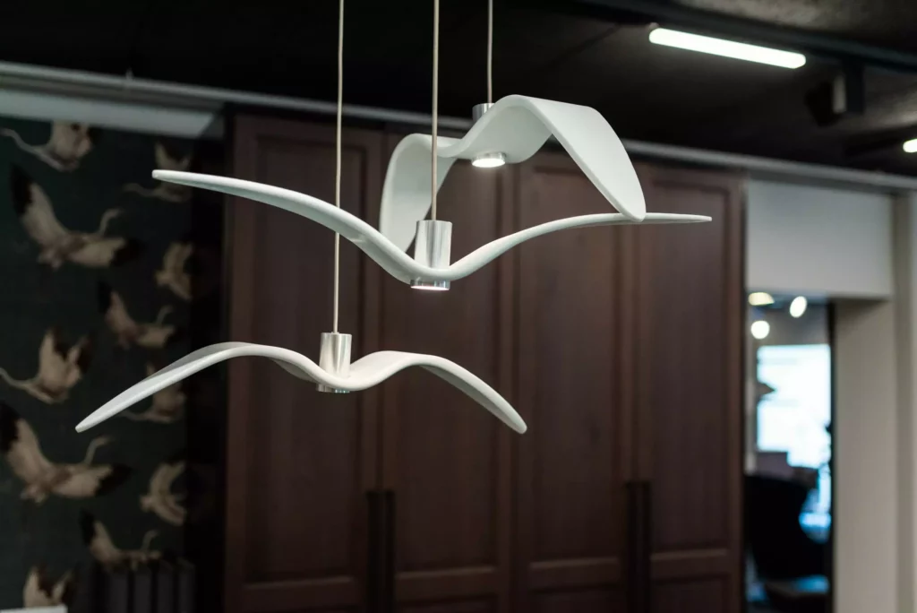 Moderne weiße Designer-Hängelampen in Form von Vögeln im Möbelstudio-Showroom mit dunklen Holzschränken im Hintergrund