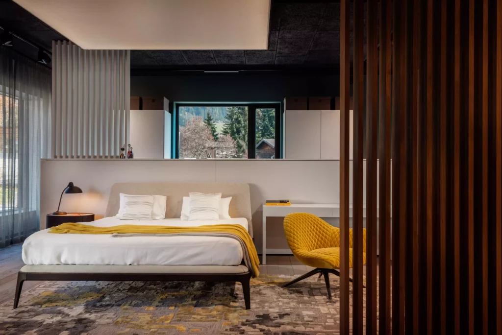 Moderner Showroom mit Bett, gelbem Designersessel, Teppich und Blick auf Natur, Innenarchitektur und Möbelstudio Ambiente