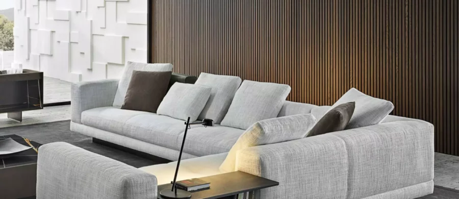 Modernes Wohnzimmer mit grauem Minotti Sofa, integriertem Beistelltisch, Leselampe und dunklem Teppich vor Holzpaneelwand