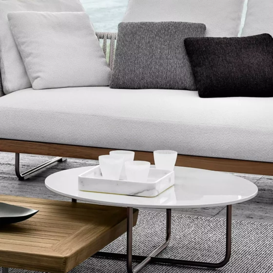 Moderner Minotti Sofa mit grauen Kissen und zwei Couchtischen aus Holz und weißem Glas im Showroom mit Meerblick