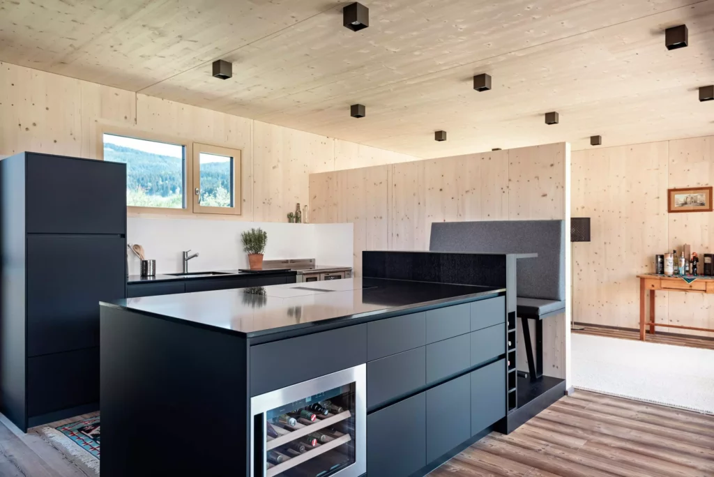 Moderne Poliform Küche Alea in mattem Schwarz mit Kochinsel, Weinkühler und Sitzbank in hellem Holzraum mit Panoramafenster
