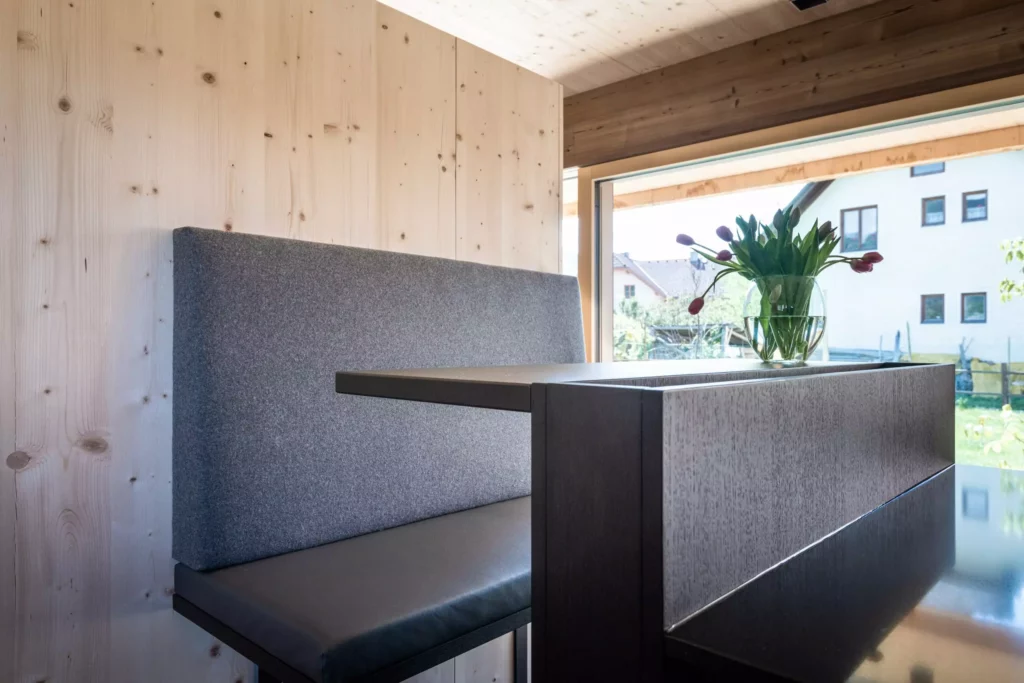 Moderne Poliform Küche mit grauer Polsterbank, dunklem Holz-Tisch und Fensterfront mit Blick ins Grüne in Salzburg