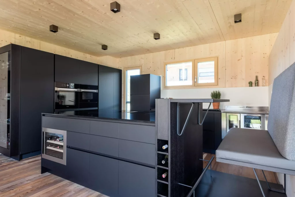 Moderne Poliform Küche in Salzburg mit schwarzer Insel, integrierter Weinkühlung, Sitzbank und Holzverkleidung als