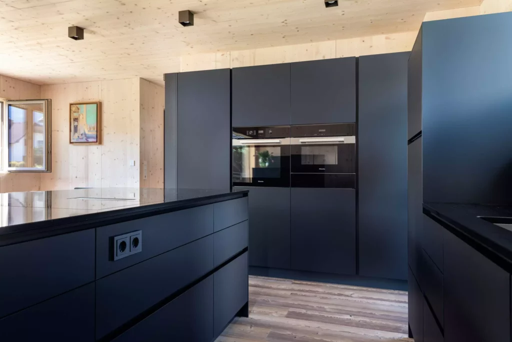 Moderne Poliform Alea Küche in mattem Schwarz mit Miele Einbaugeräten, Holzdecke und hellem Holzboden in Salzburg