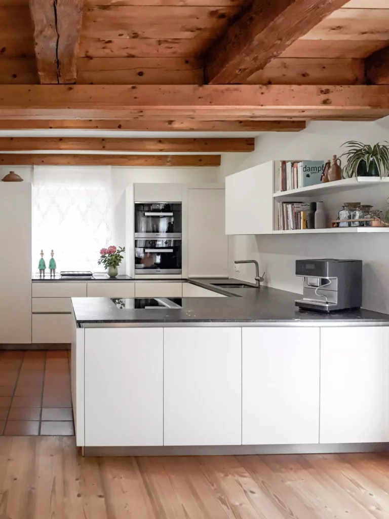 Moderne weiße Küche mit schwarzer Arbeitsplatte, eingebauten Miele Geräten, Holzdecke und offenem Regal mit, Selectiond