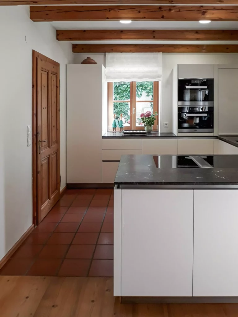 Moderne weiße Küche mit Miele Backofen, Kochinsel mit schwarzer Arbeitsplatte, Holzdecke und Fenster mit Blick, Selectiond