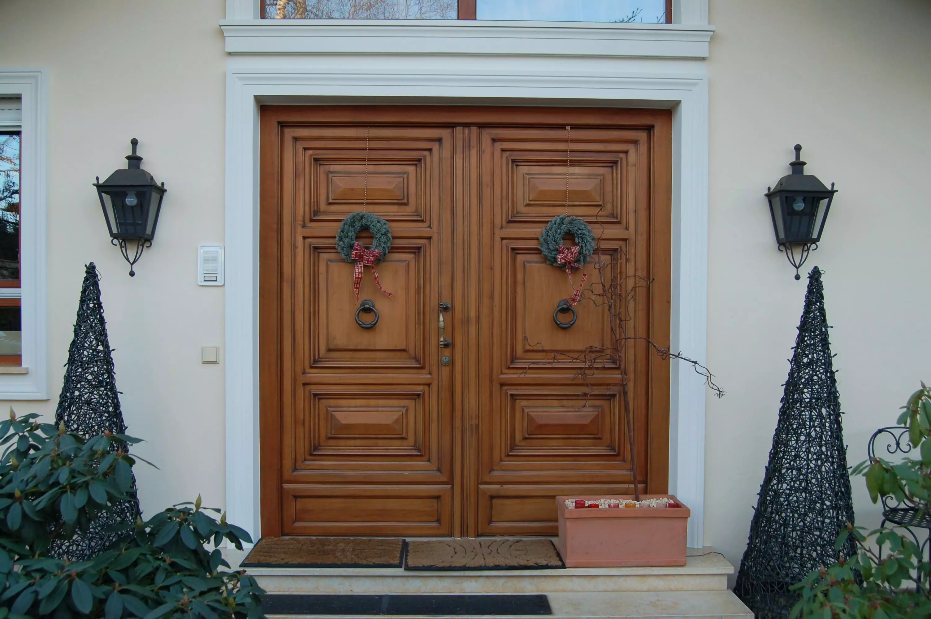 Doppelflügelige Holztür mit dekorativen Kränzen, flankiert von zwei schwarzen Laternen und zwei konischen, Weitgasser