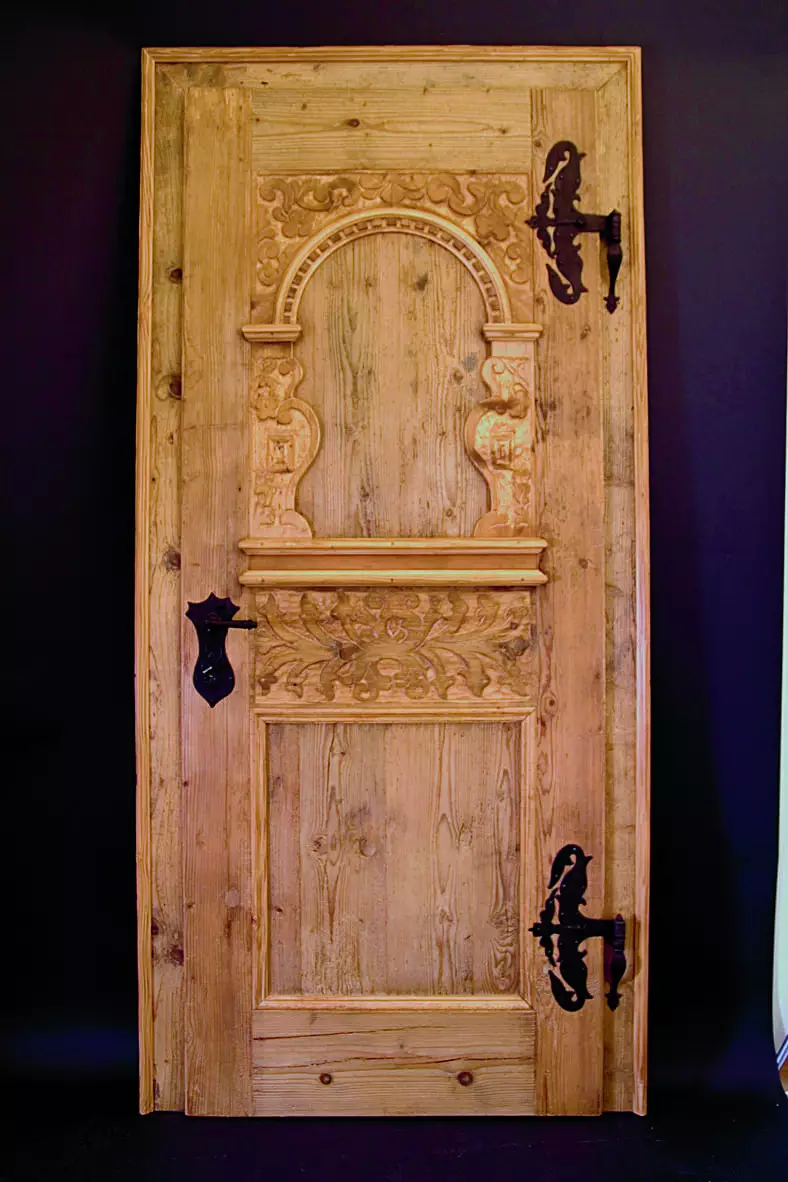 Antike Holztür mit aufwendigen Schnitzereien und schmiedeeisernen Beschlägen, präsentiert von Tischlerei Weitgasser