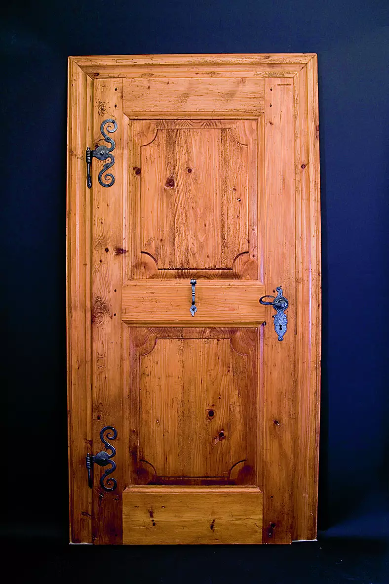 Antike Holztür mit dekorativen Metallbeschlägen vor dunklem Hintergrund, Tischlerei Weitgasser Altenmarkt