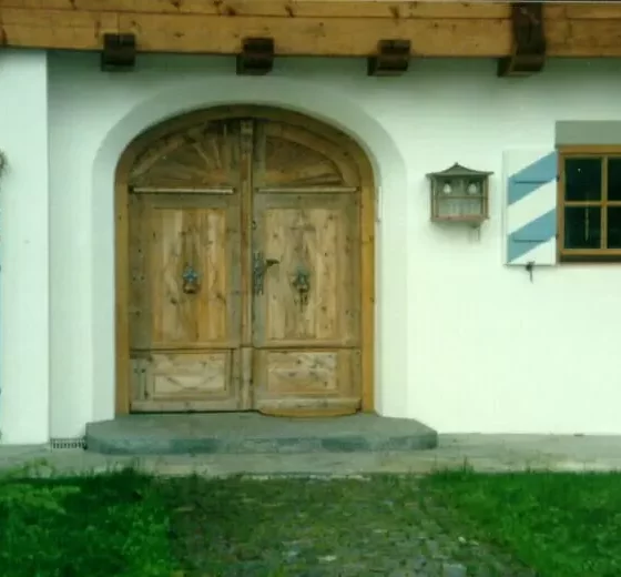 Holztür mit Rundbogen und dekorativen Beschlägen an weißem Haus mit Fenster und blauen Fensterläden, Türelement, Weitgasser
