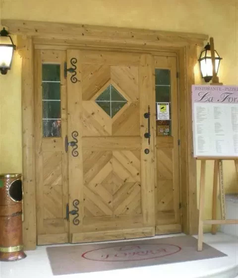 Eingangstür aus Holz mit dekorativen Eisenbeschlägen und Glaseinsätzen, daneben ein Menüständer vor gelber Wand, Weitgasser