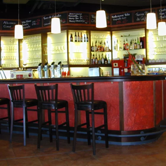 Bar mit rotem Tresen, schwarzen Barhockern und beleuchteten Regalen mit Gläsern und Spirituosen, moderne, Weitgasser