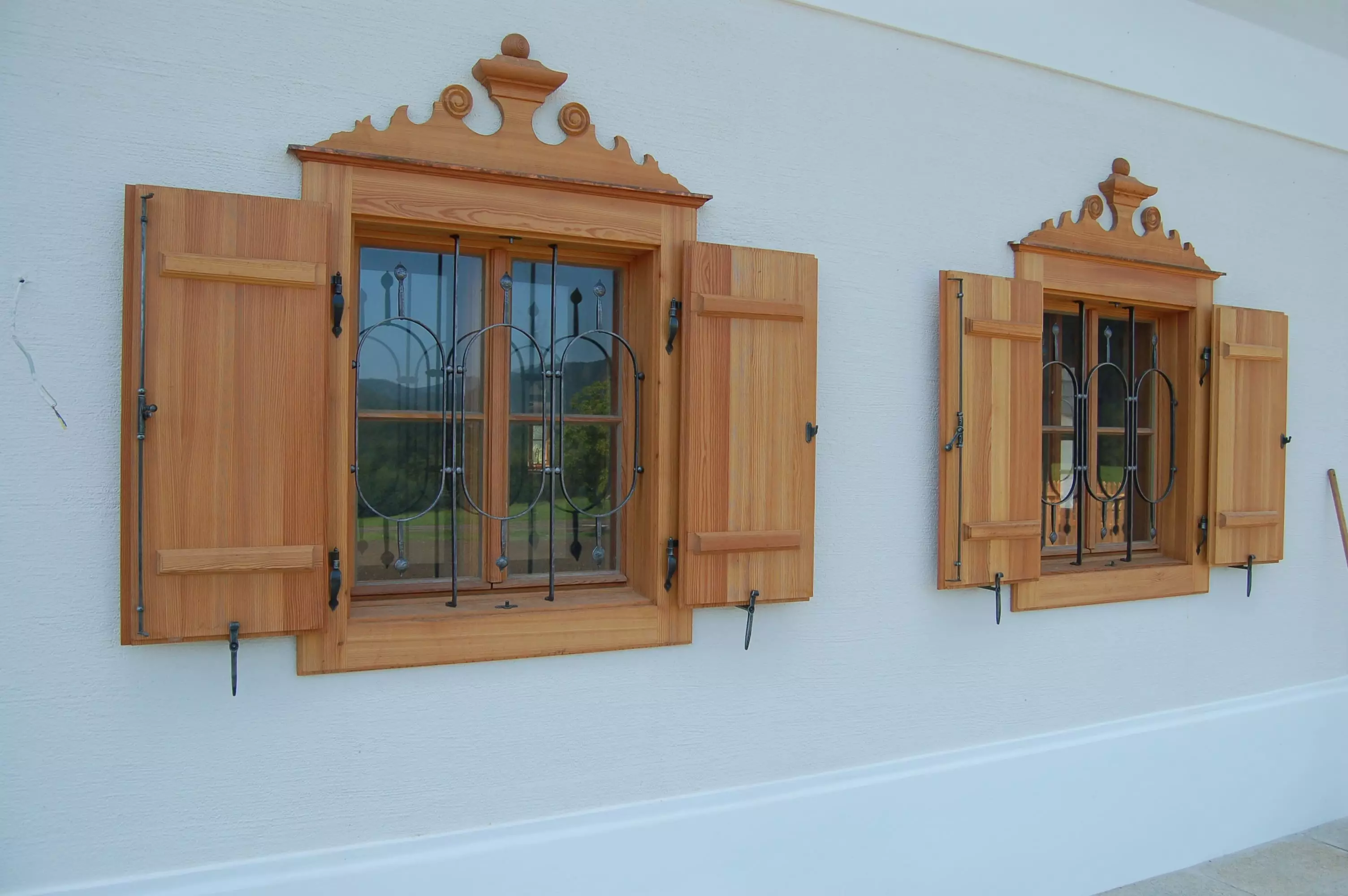 Zwei handgefertigte Kastenfenster aus Holz mit dekorativen Fensterläden und schmiedeeisernem Gitter an weißer, Weitgasser