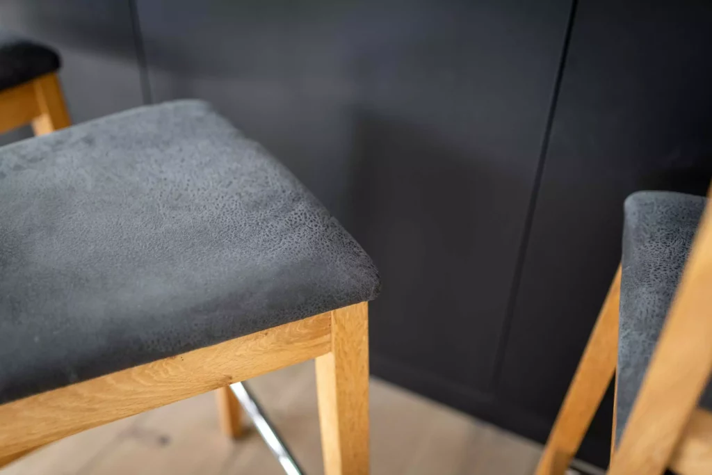 Nahaufnahme von zwei Holzstühlen mit grauen Sitzpolstern vor schwarzem Wandverbau in moderner Tischlereiküche, Tischlerküche