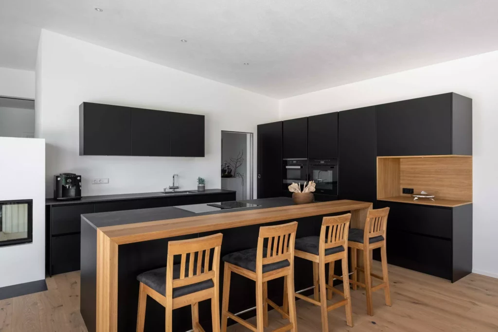 Moderne Tischlereiküche mit schwarzer Front, Holztheke und vier Holzbarhockern, integriertem Kochfeld und, Tischlerküche