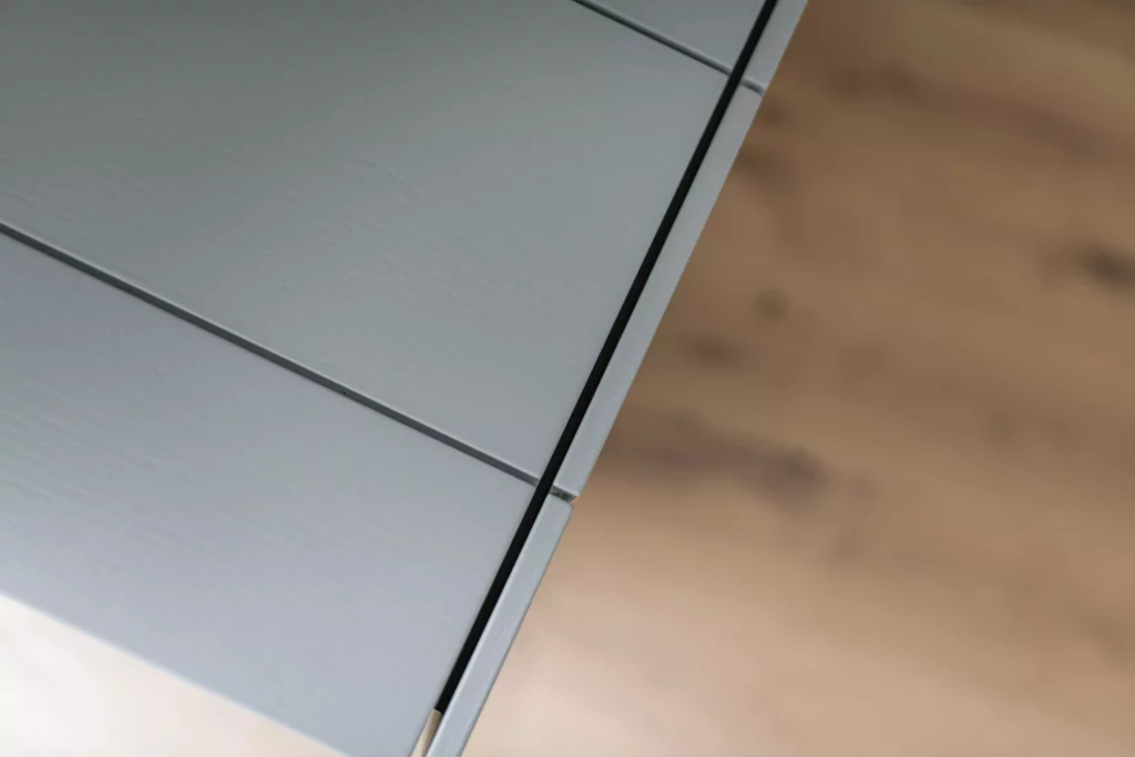 Detailaufnahme einer grauen Tischlereiküche mit sichtbarer Holzmaserung und präziser Fuge, Boden aus hellem, Tischlerküche