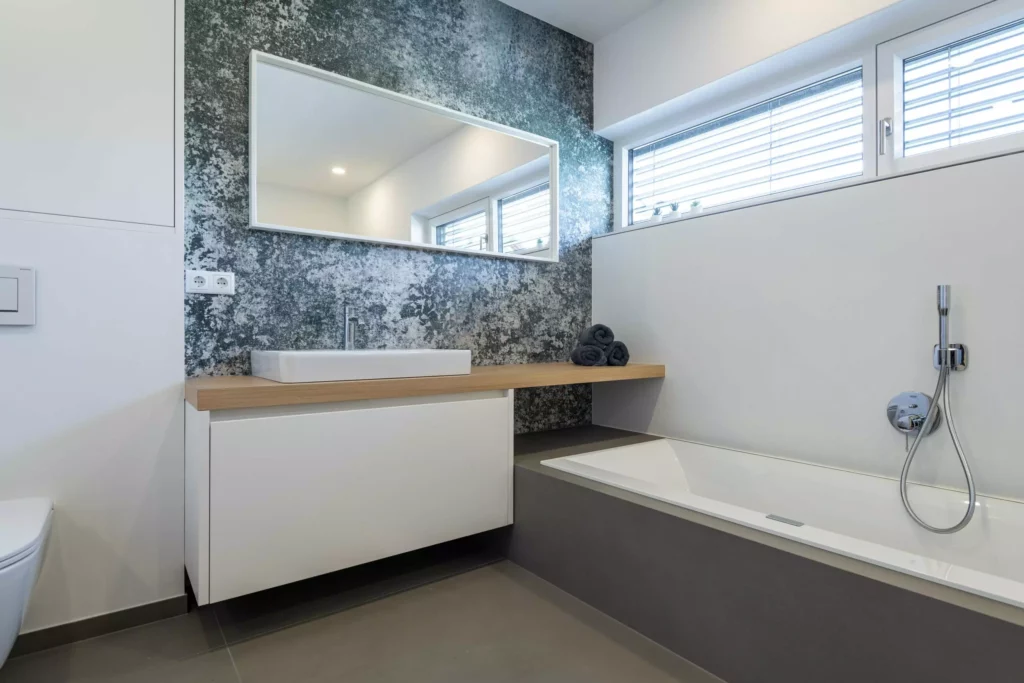 Modernes Badezimmer mit maßgefertigtem Waschtisch aus Holz, großem Spiegel, Badewanne und grauer Akzentwand, Tischlerküche
