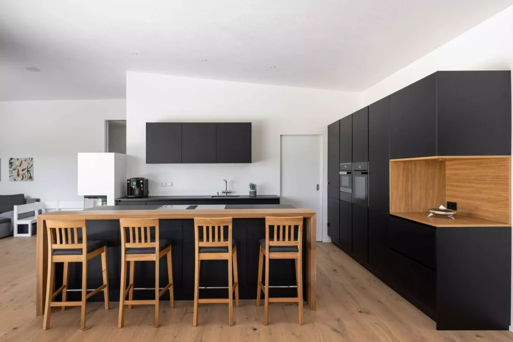 Moderne maßgefertigte Tischlerküche mit schwarzer Front, Holzarbeitsplatte, Kücheninsel mit Barhockern und integriertem