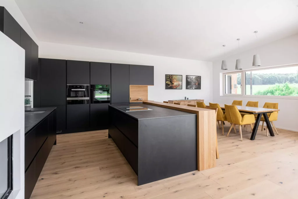 Moderne Tischlereiküche mit schwarzer Front, Kochinsel mit Holzabschluss und angrenzendem Essbereich mit, Tischlerküche