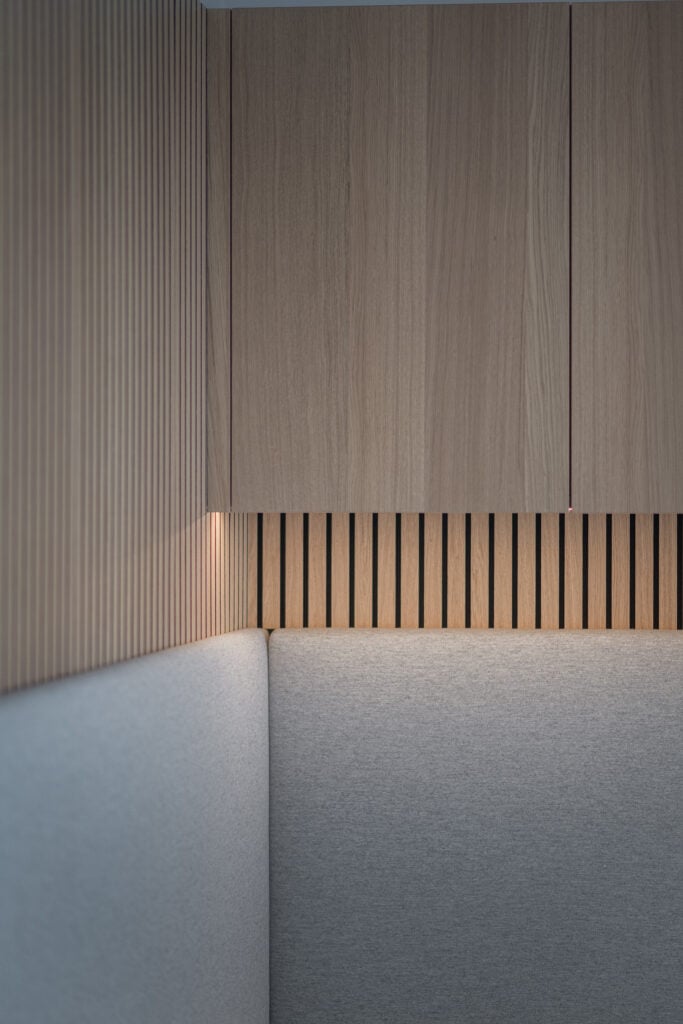 Ecke einer modernen Innenraumlösung mit grauem Polster, vertikalen Holzlamellen und schwebenden Holzschränken, Einrichtung