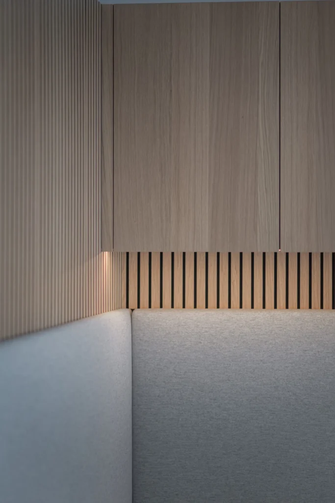 Ecke einer modernen Innenraumlösung mit grauem Polster, vertikalen Holzlamellen und schwebenden Holzschränken, Einrichtung