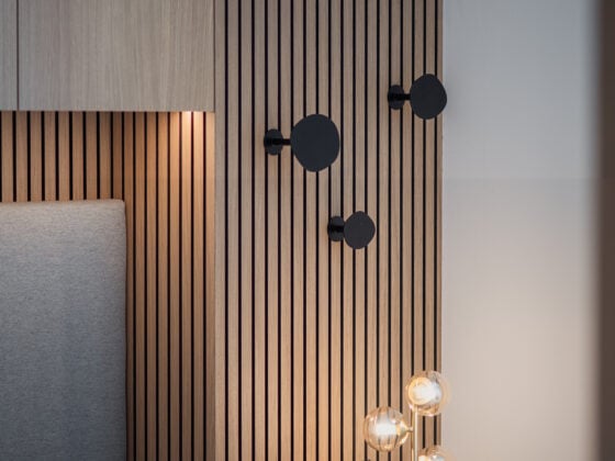 Moderner Schlafzimmerbereich mit grauem Polsterbett, Holzpaneelwand mit schwarzen Haken und Design-Tischleuchte, Einrichtung