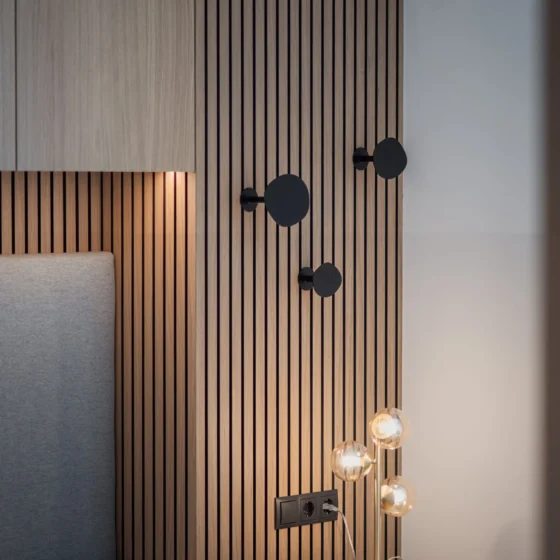 Moderner Schlafzimmerbereich mit grauem Polsterbett, Holzpaneelwand mit schwarzen Haken und Design-Tischleuchte, Einrichtung