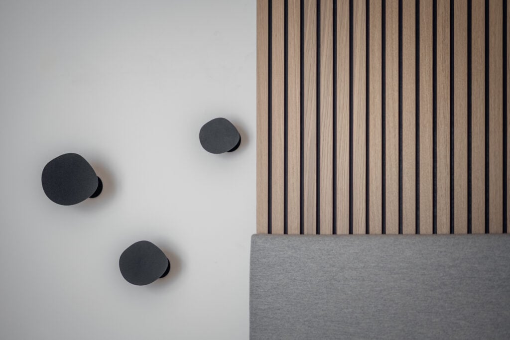 Minimalistisches Schlafzimmer mit grauem Polsterbett, Holzlamellenwand und drei schwarzen Wandhaken in, Einrichtung