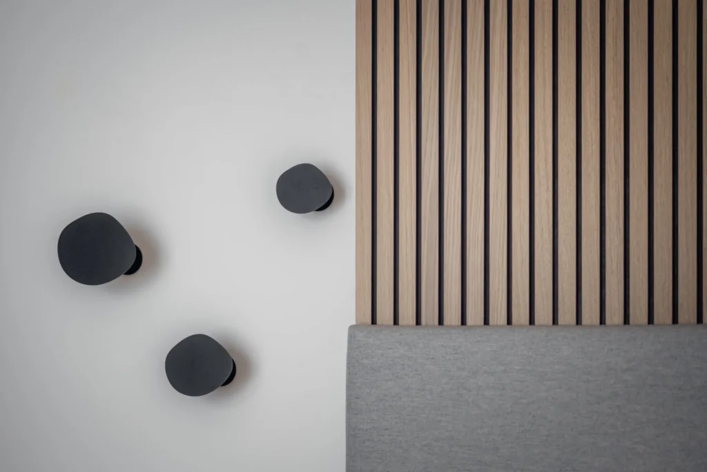 Minimalistisches Schlafzimmer mit grauem Polsterbett, Holzlamellenwand und drei schwarzen Wandhaken in, Einrichtung