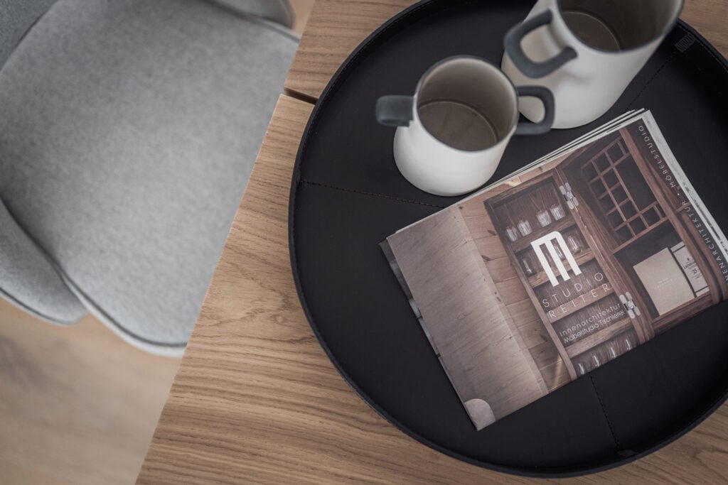 Nahaufnahme eines runden schwarzen Tabletts mit zwei weißen Tassen und einer Broschüre von Studio Reiter auf, Einrichtung