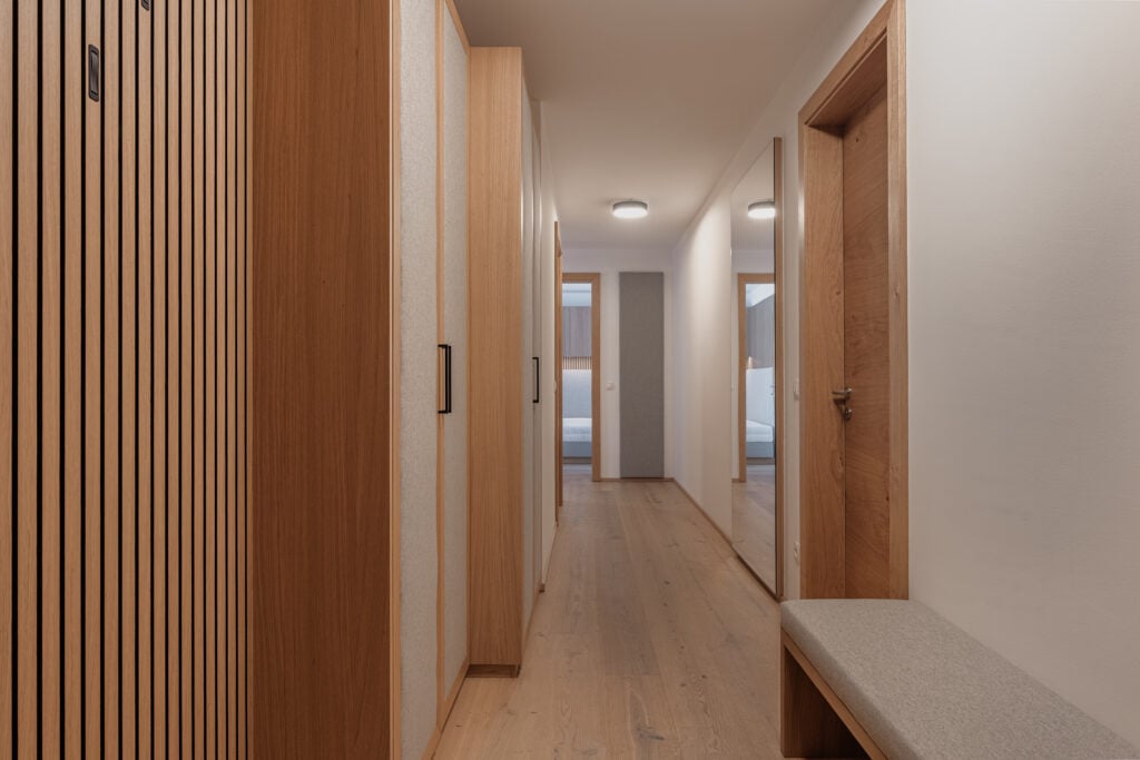 Flur mit maßgefertigten Holzeinbauten, Sitzbank mit grauem Polster, großem Wandspiegel und Türen zu, Einrichtung