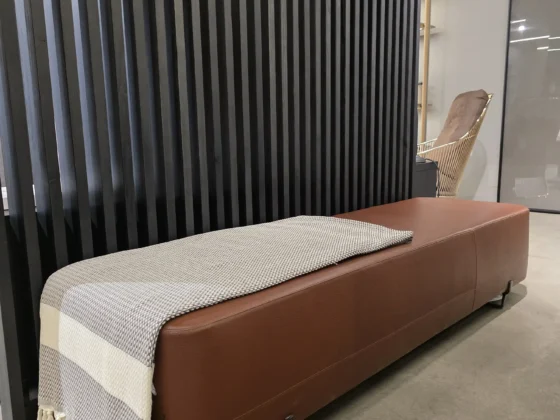 Braune Lederbank mit grauer Decke vor schwarzer Lamellenwand im modernen Möbelstudio Showroom, Scaled