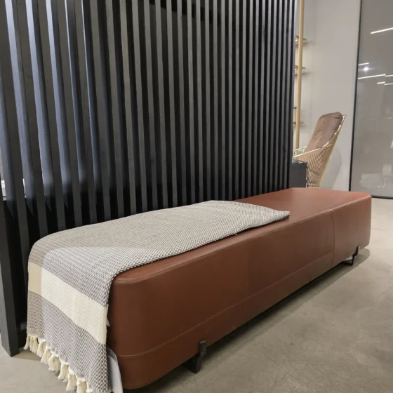 Braune Lederbank mit grauer Decke vor schwarzer Lamellenwand im modernen Möbelstudio Showroom, Scaled