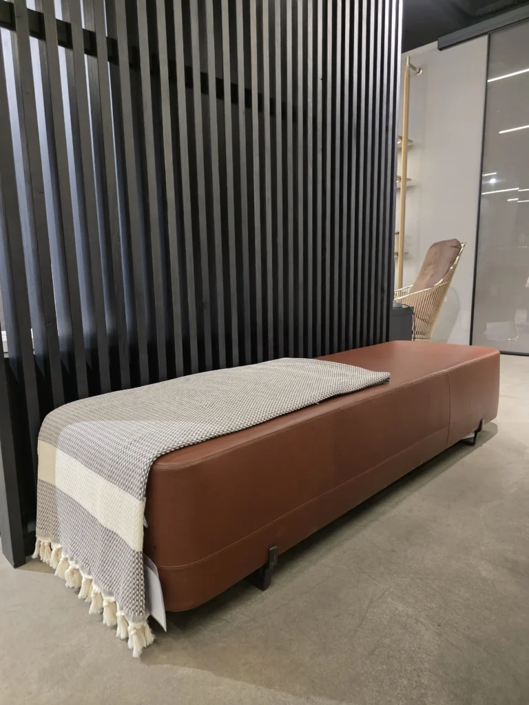Braune Lederbank mit grauer Decke vor schwarzer Lamellenwand im modernen Möbelstudio Showroom, Scaled