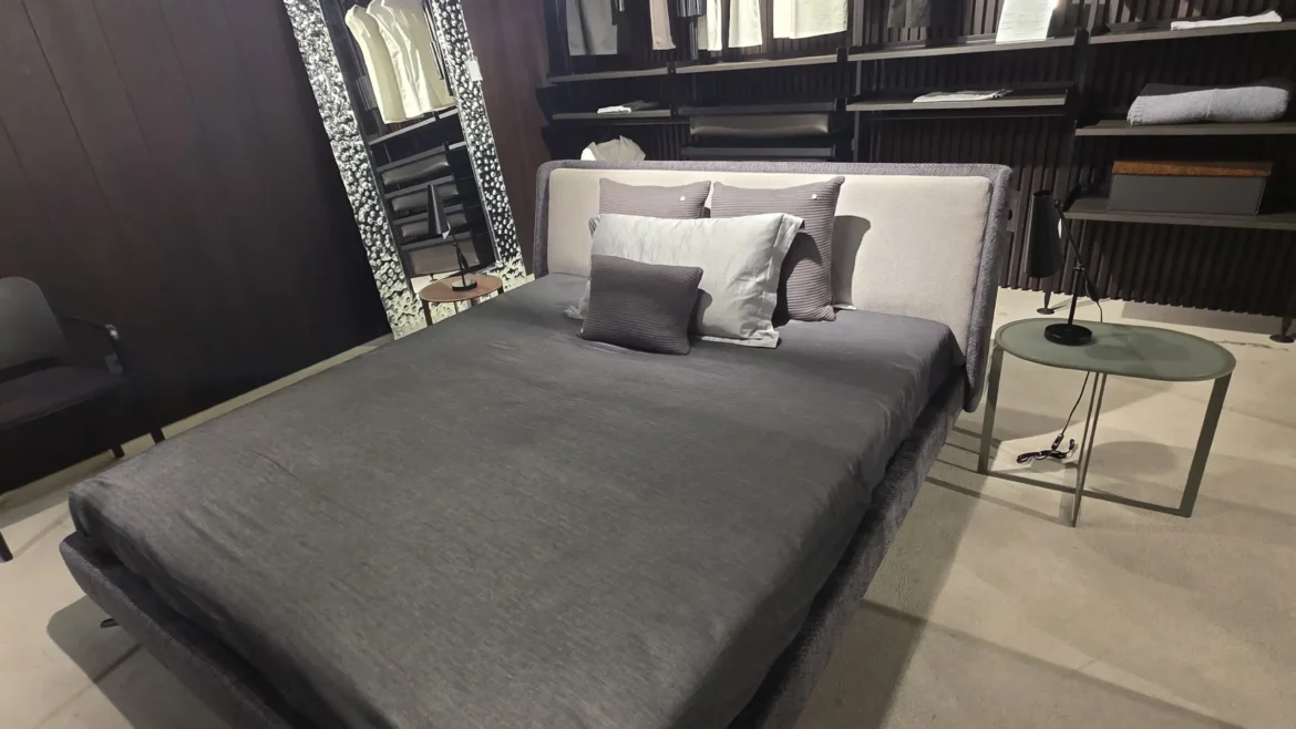Modernes Minotti Bett mit grauer Bettwäsche und Kissen in einem stilvollen Showroom mit Designermöbeln und Raumlösung