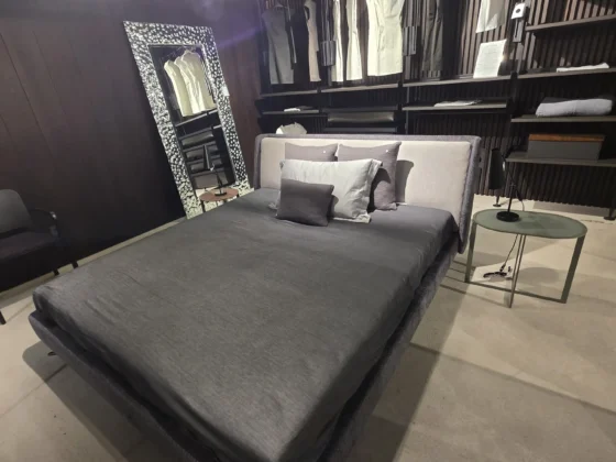 Modernes Minotti Bett mit grauer Bettwäsche und Kissen in einem stilvollen Showroom mit Designermöbeln und Raumlösung