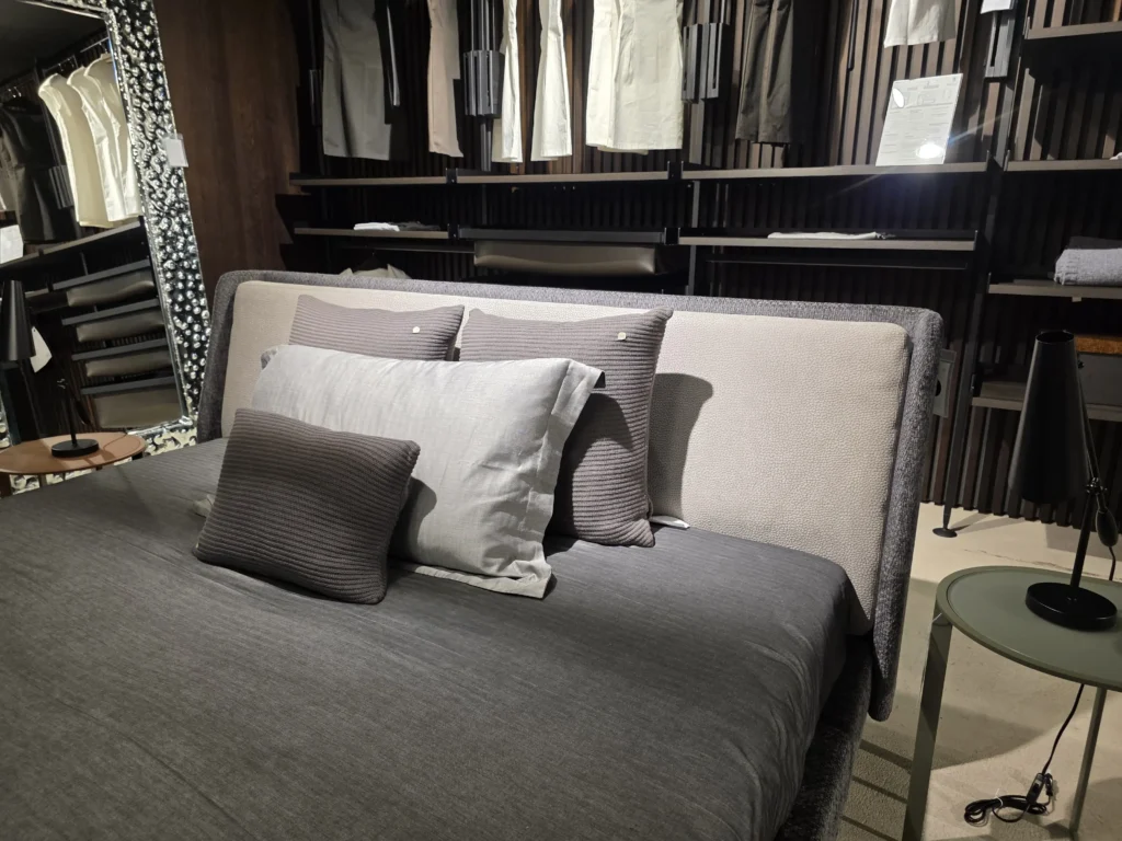 Minotti Bett mit grauer Bettwäsche und Kissen im modernen Showroom für Innenarchitektur und Designermöbel