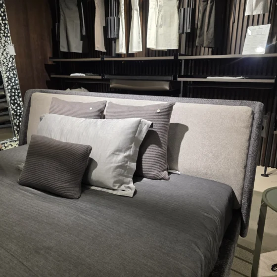 Minotti Bett mit grauer Bettwäsche und Kissen im modernen Showroom für Innenarchitektur und Designermöbel