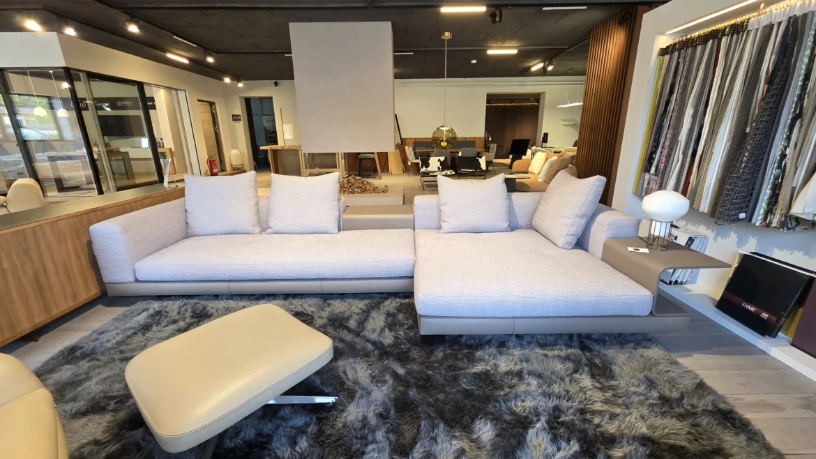 Modernes Minotti Connery Sofa mit hellgrauem Stoffbezug und integriertem Beistelltisch im Möbelstudio mit Teppich und