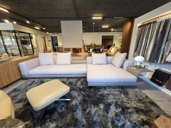 Modernes Minotti Connery Sofa mit hellgrauem Stoffbezug und integriertem Beistelltisch im Möbelstudio mit Teppich und